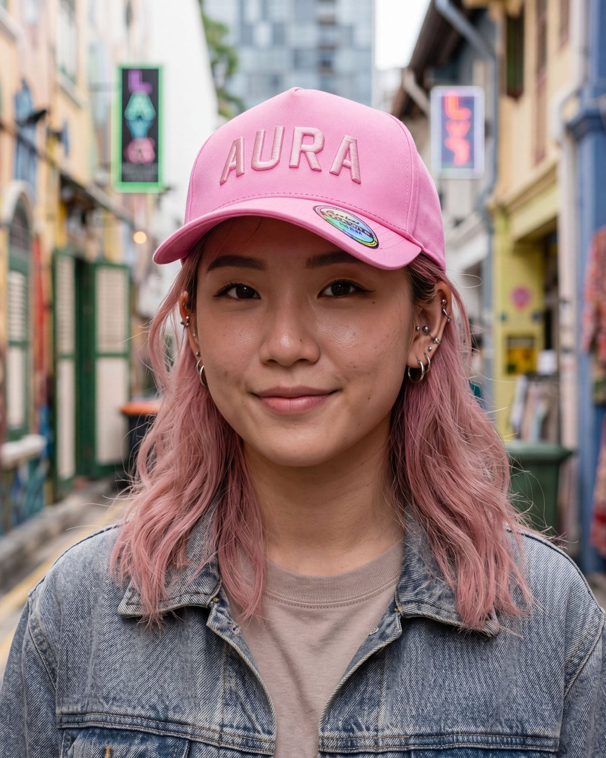 Person wearing a pink 'Aura' cap in an urban setting