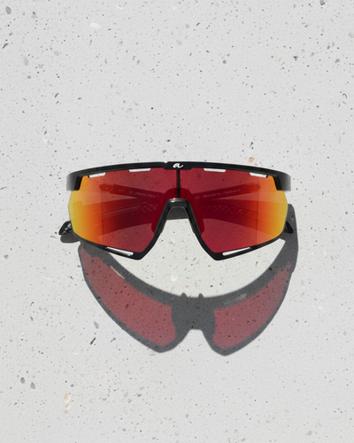 Sunglasses with red-tinted lenses on a light gray surface