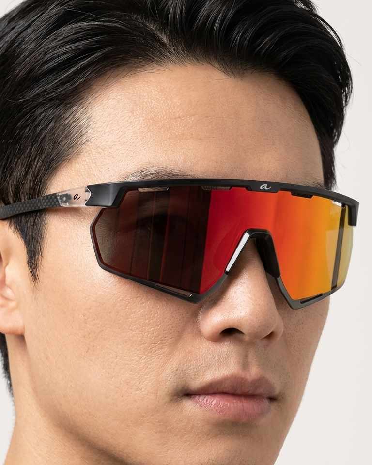 Person wearing a pair of sunglasses with a reflective red lens on a neutral background